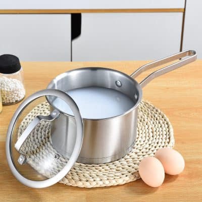 Creamy liquid in stainless steel saucepan with lid on woven placemat, eggs and condiments on wooden table, kitchen cookware with milk, cooking, kitchen utensils, food preparation, Monalisa Store.