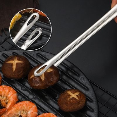 Stainless steel tongs with a textured grip handling grilled mushrooms and shrimp on a black grill pan, ideal for cooking and serving seafood and vegetables with precision.