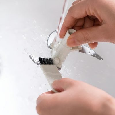 Light-skinned hands cleaning a small toy airplane under running water in a sink, focusing on sanitation and hygiene.