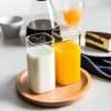 Cream and orange juice in glass bottles on wooden tray, with coffee, cake, and breakfast items in background. Perfect for healthy breakfast or brunch images.
