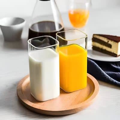 Cream and orange juice in glass bottles on wooden tray, with coffee, cake, and breakfast items in background. Perfect for healthy breakfast or brunch images.