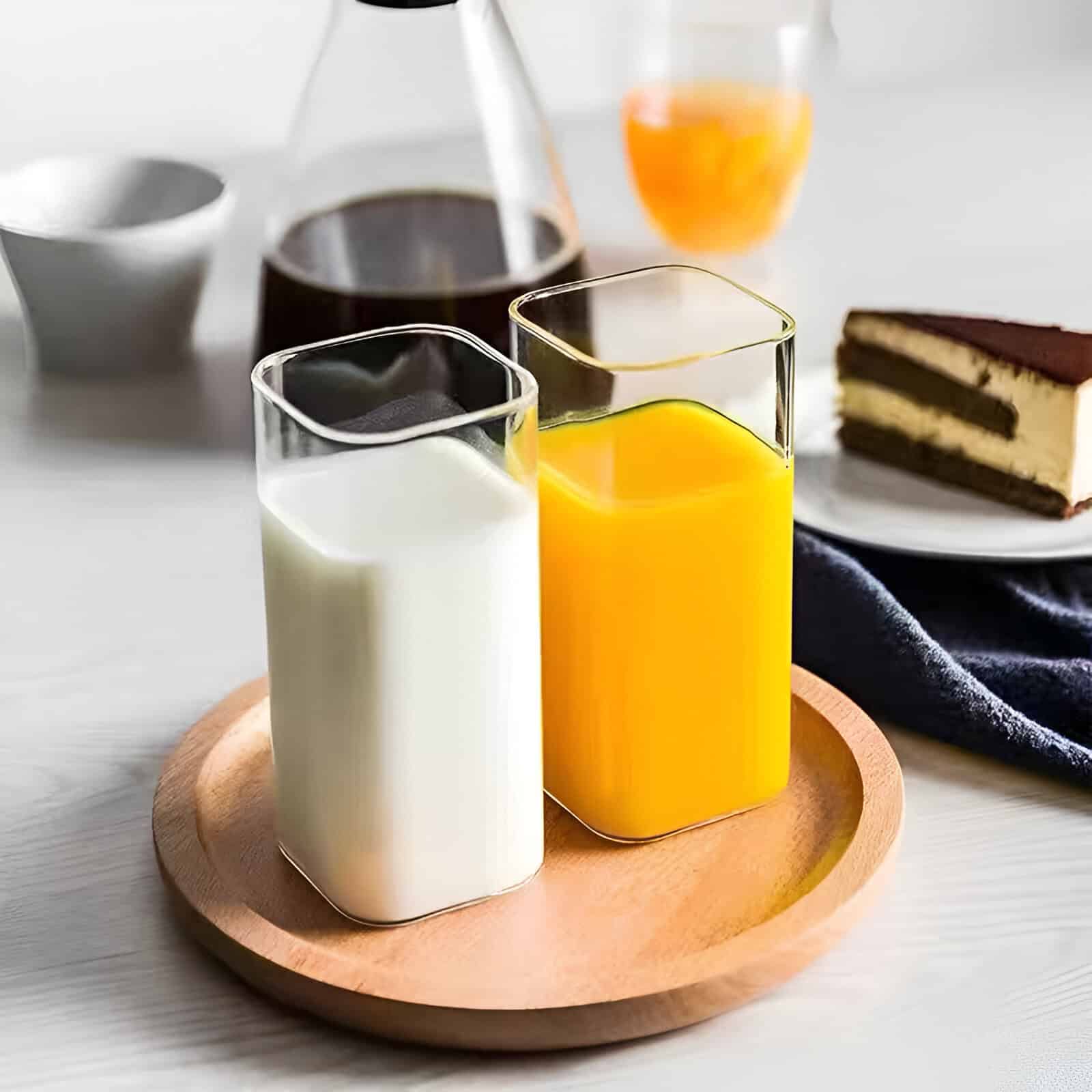 Cream and orange juice in glass bottles on wooden tray, with coffee, cake, and breakfast items in background. Perfect for healthy breakfast or brunch images.