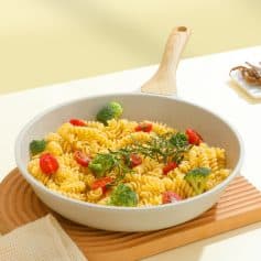 Crispy pasta with cherry tomatoes and broccoli in a white skillet on wooden tray.