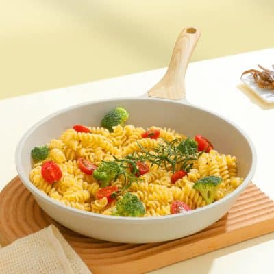 Crispy pasta with cherry tomatoes and broccoli in a white skillet on wooden tray.