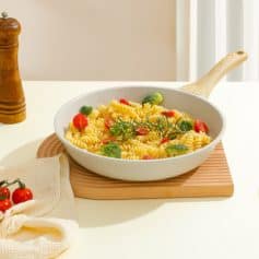 Vegan pasta with cherry tomatoes broccoli and herbs in a white skillet on wooden cutting board at Monalisa Store.