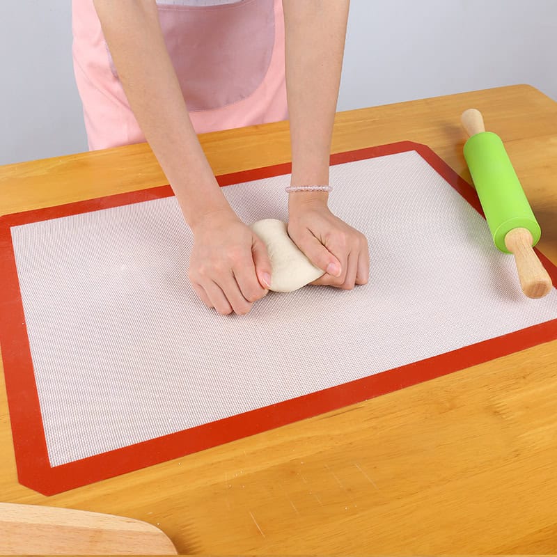 Freshly baked bread dough being kneaded on a silicone baking mat, with a green rolling pin nearby. Perfect for homemade baking and bread-making at home.