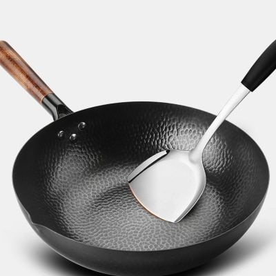 Polished black cast iron frying pan with wooden handle and metal spatula, ideal for cooking and kitchen use.