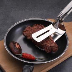Grill pan with cooked steak, shiitake mushroom, and red chili pepper on wooden cutting board, showcasing kitchen cookware and food preparation.