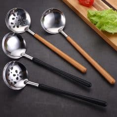 Stainless steel slotted and solid cooking spoons with wooden and black handles, professional kitchen utensils for cooking and serving.