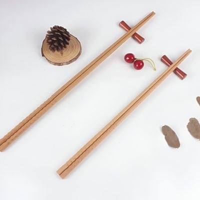 Elegant wooden chopsticks with red handles, decorative pinecone, cherries, and natural elements on a white background, suitable for stylish dining and cultural cuisine displays.