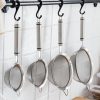 Stainless steel mesh strainers hanging on a kitchen rack against white tiled wall.