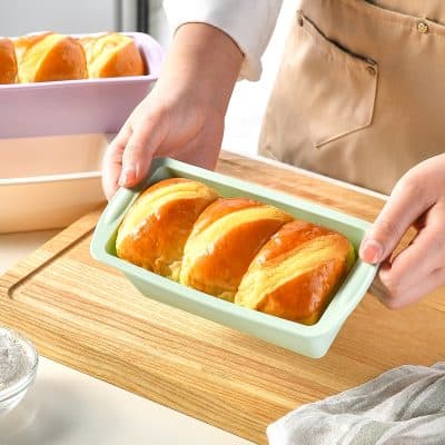 Fluffy baked bread rolls in a green container, close-up, fresh and golden, perfect for breakfast or snack, soft and delicious baked goods.