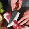 Santoku knife slicing raw meat on cutting board with vegetables and lemon in background, high quality image for cooking and kitchen tools, Monalisa Store.