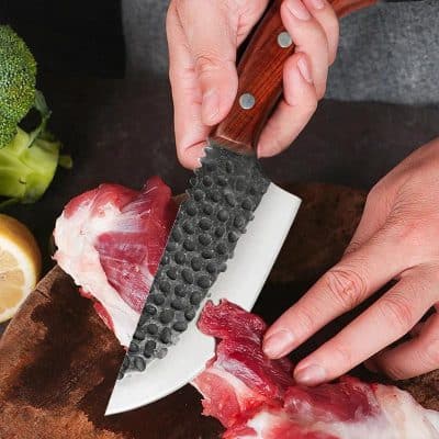 Santoku knife slicing raw meat on cutting board with vegetables and lemon in background, high quality image for cooking and kitchen tools, Monalisa Store.