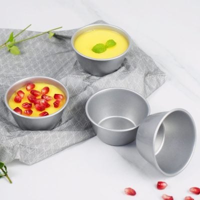 Pomegranate and lemon custard in metal baking cups on a gray cloth, with empty cups nearby, for baking or dessert presentation.