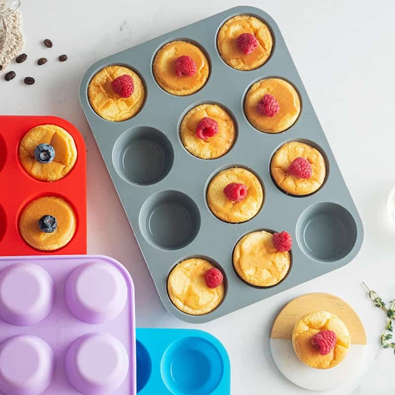 Freshly baked muffins with raspberries and blueberries in colorful silicone molds, perfect for breakfast or snack, displayed on a clean kitchen surface.