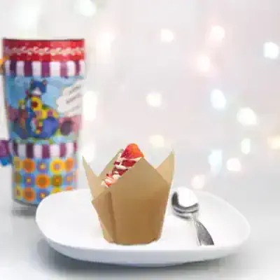 Colorful child's yogurt cup with cartoon character design, placed near a white plate with a fresh strawberry, on a surface with bokeh lights background, promoting healthy snacks at Monalisa Medical.