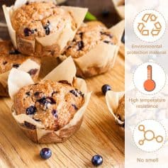 Golden blueberry muffins in parchment paper liners on wooden surface, fresh blueberries scattered around.