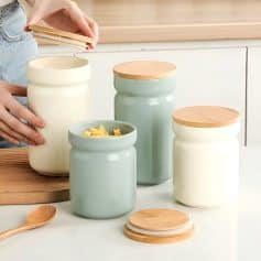 Cream-colored and pastel green storage jars with wooden lids, perfect for kitchen organization and food storage, featured on Monalisa Store.