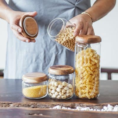 Assorted dry pasta stored in glass jars with wooden lids on a rustic wooden table.