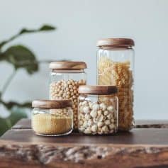Assorted glass jars with wooden lids containing pasta and grains on a wooden surface at Monalisa Store.