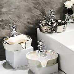 Shiny silver and pearl-colored ceramic sink bowls with decorative faucet fixtures, displayed on white pedestals in a modern bathroom setting.