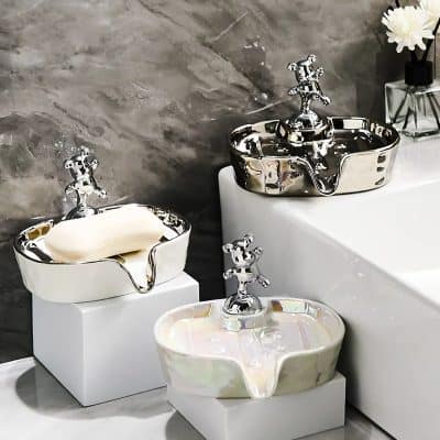 Shiny silver and pearl-colored ceramic sink bowls with decorative faucet fixtures, displayed on white pedestals in a modern bathroom setting.