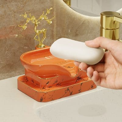 Elegant orange marble soap dish with a golden deer sculpture in the background, perfect for luxury bathroom decor.