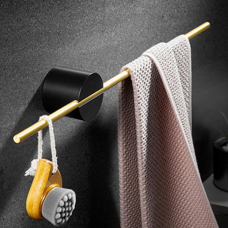 Cleaning brush hanging on a gold towel rack with a pink textured towel draped over it in a modern bathroom setting.