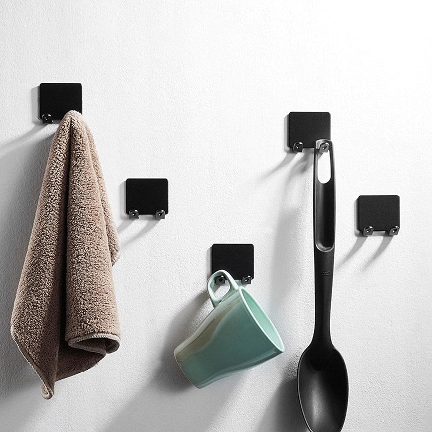 Neat wall hooks for organizing kitchen or bathroom essentials, featuring a black minimalist design with a towel, mug, and ladle hanging on a white wall. Perfect for modern space organization.
