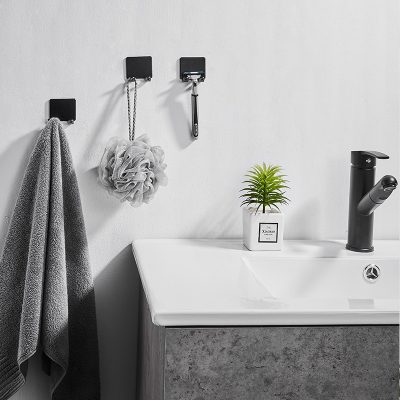 Soft gray towel hanging in a modern bathroom with hooks, a cleaning sponge, a small potted plant, and a black sink faucet for stylish bathroom and skincare essentials.