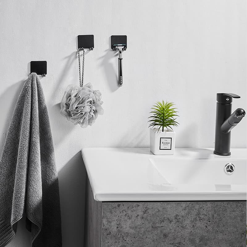 Soft gray towel hanging in a modern bathroom with hooks, a cleaning sponge, a small potted plant, and a black sink faucet for stylish bathroom and skincare essentials.