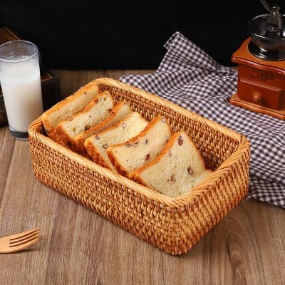 Soft raisin bread slices in a wicker basket, with a glass of milk, coffee grinder, and checkered cloth in the background, ideal for breakfast or snack.