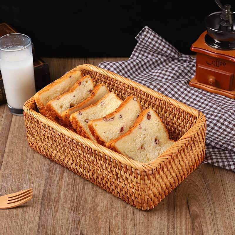 Soft raisin bread slices in a wicker basket, with a glass of milk, coffee grinder, and checkered cloth in the background, ideal for breakfast or snack.