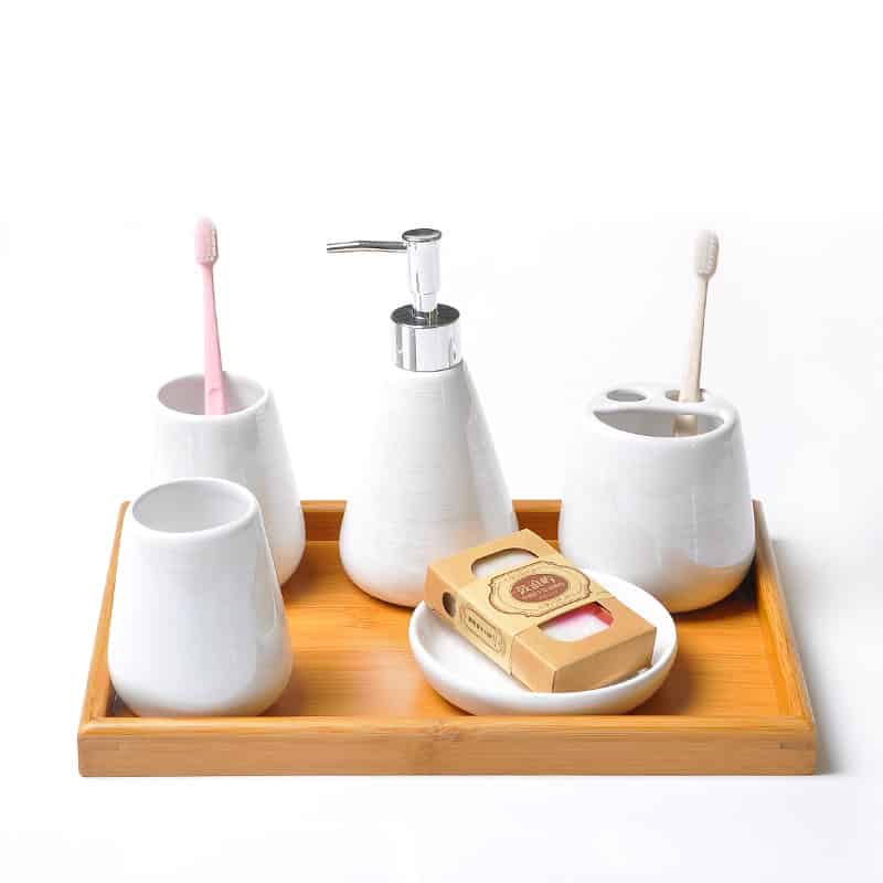 Toothbrush holder set with ceramic cups, soap dispenser, and natural soap on a wooden tray for dental hygiene.