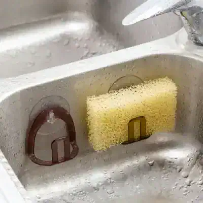 Cleaning sponge and scrubber holder in kitchen sink, organized for dishwashing chores, focusing on kitchen cleaning tools, sponge storage, and sink accessories.