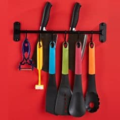 Colorful kitchen spatulas and tools hanging on a black wall rack against a red background, perfect for cooking and household needs.