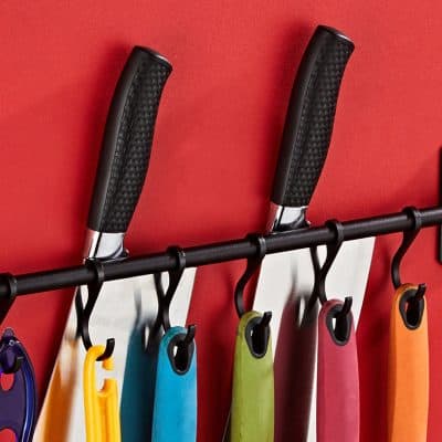 Colorful kitchen knives hanging on a magnetic strip with red wall background at Monalisa Medical Store.