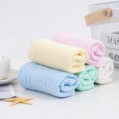 Soft pastel-colored towels stacked on a white surface with bathroom accessories, perfect for spa or skincare routines.