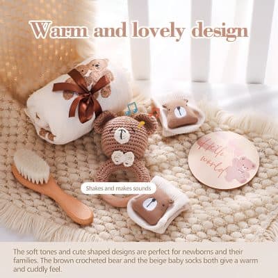 Soft baby care items including crocheted bear and plush baby socks with teddy bear designs, wooden brush, and greeting card, emphasizing warmth and cuddly textures perfect for newborns and families.