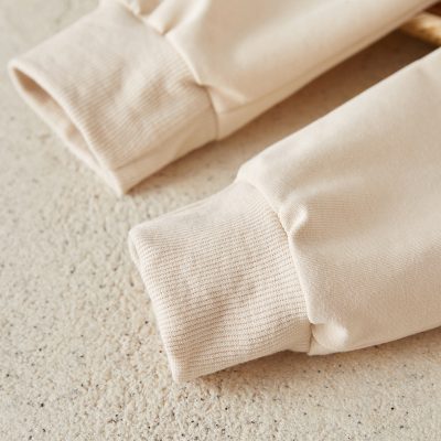 Comfy beige sweatshirt cuffs on neutral textured surface, casual style, warm cozy clothing, loungewear, soft fabric, minimalistic fashion, relaxed fit, everyday wear.