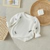 Soft white knitted baby sweater with black stripe details, perfect for comfortable and stylish infant wear.