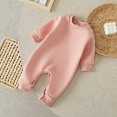 Plush pink baby romper with snap buttons on shoulder and foot closures, ideal for infant comfort and warmth, displayed on a neutral textured surface with natural decor elements.