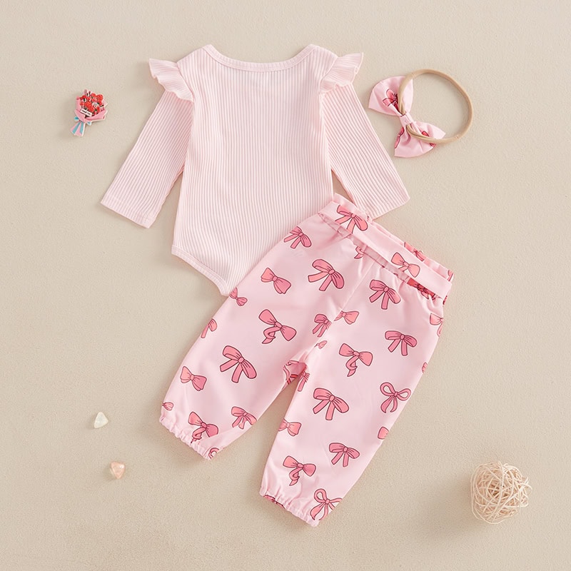 Pink baby outfit with a ribbed long-sleeve top and bow-print pants, accessories include a headband and small decorative hearts on a neutral background. Perfect for infants, stylish and comfortable.