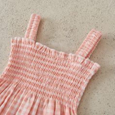 Light pink checkered smocked dress with adjustable straps, perfect for spring or summer wear, made from soft, breathable fabric for comfortable everyday use.