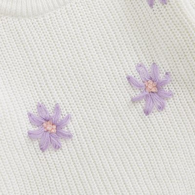 Delicate white knit fabric with embroidered lavender and pink floral details, perfect for stylish and comfortable clothing or accessories.