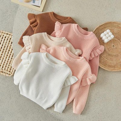 Knitted sweaters with ruffled sleeves in pastel and neutral colors, perfect for women's fashion, displayed on a textured surface at Monalisa Store.
