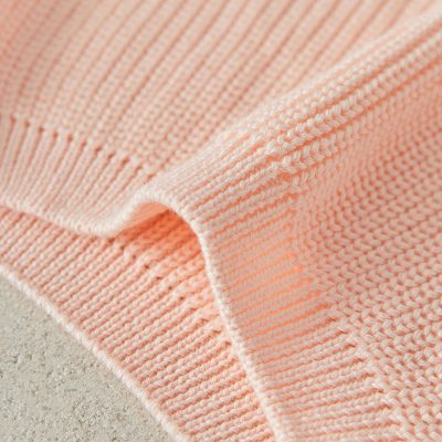 Soft peach-colored knitted blanket with intricate stitching, perfect for comfort and home decor. Ideal for cozy spaces and adding a touch of elegance.