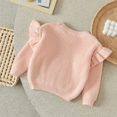 Pink children's knitted sweater with ruffled shoulder details, perfect for cozy style and comfort. Ideal for kids' fashion and casual wear.