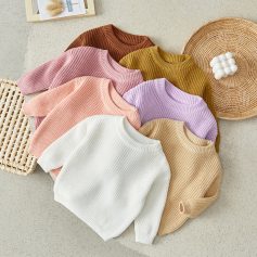 Warm knit sweaters in pastel pink, lavender, white, beige, and mustard yellow arranged on a light background.